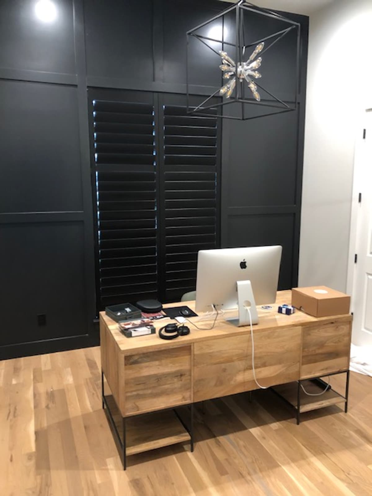 Black plantation shutters in modern home office with dark paneled walls