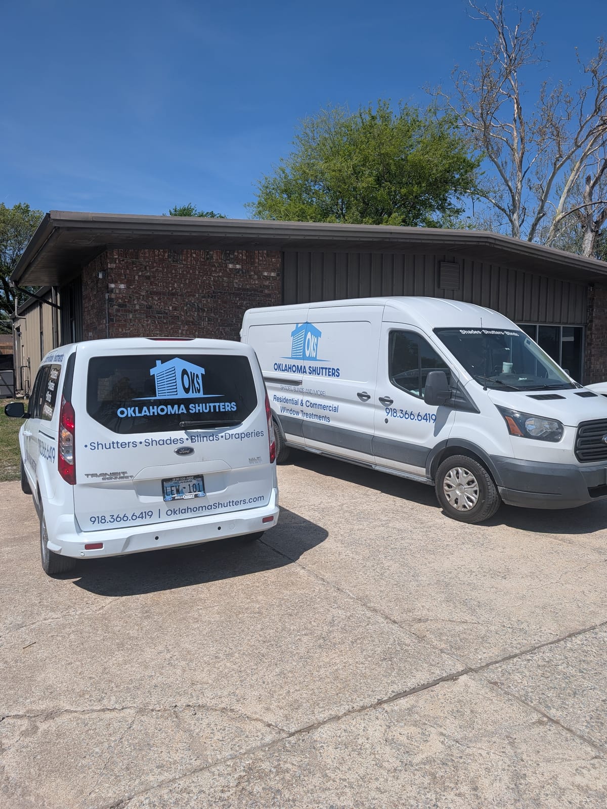Two Oklahoma Shutters service vans lettered with shutters, shades, blinds, and draperies parked outside the shop