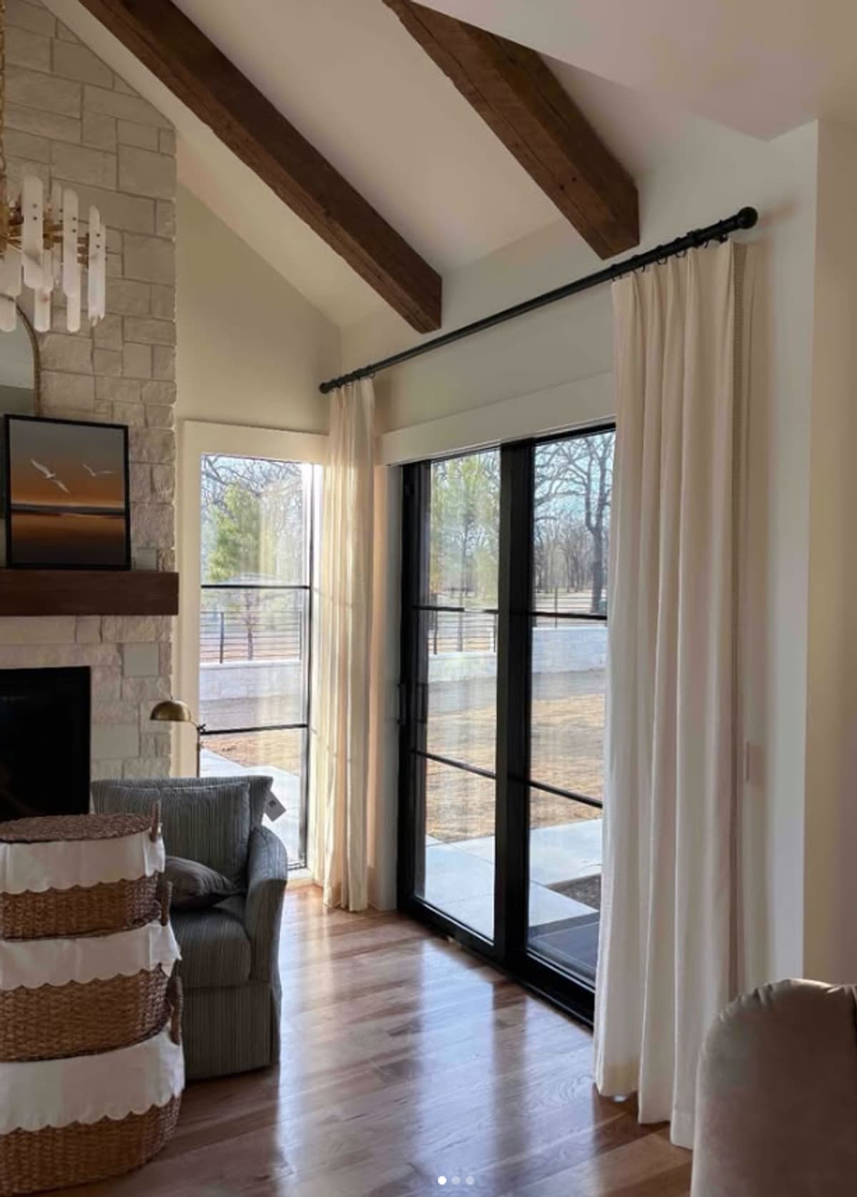 White drapery panels on black rod covering glass doors in living room with exposed beams and fireplace