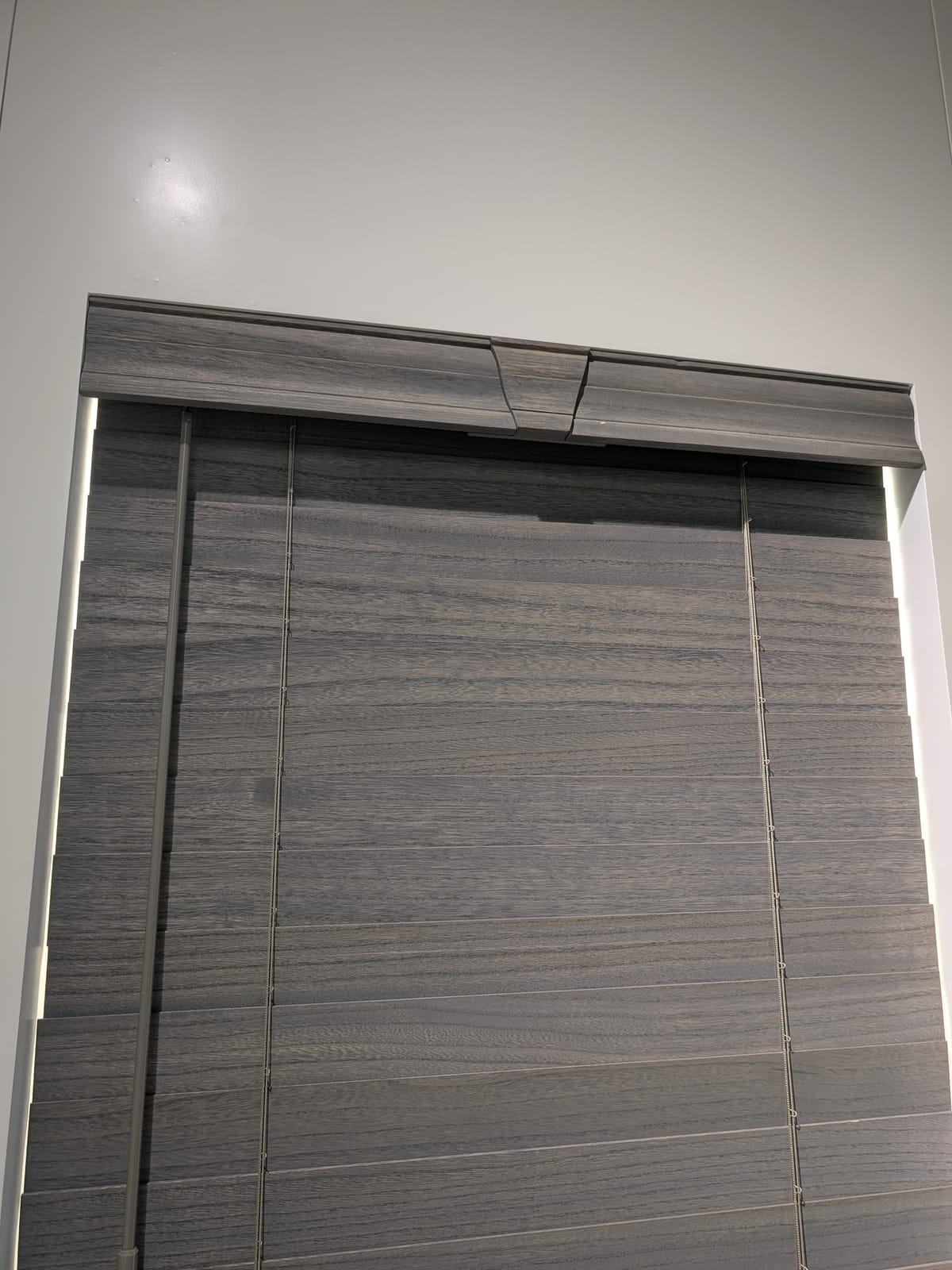 Dark gray wood-grain faux wood blinds with matching valance on a white-trimmed window