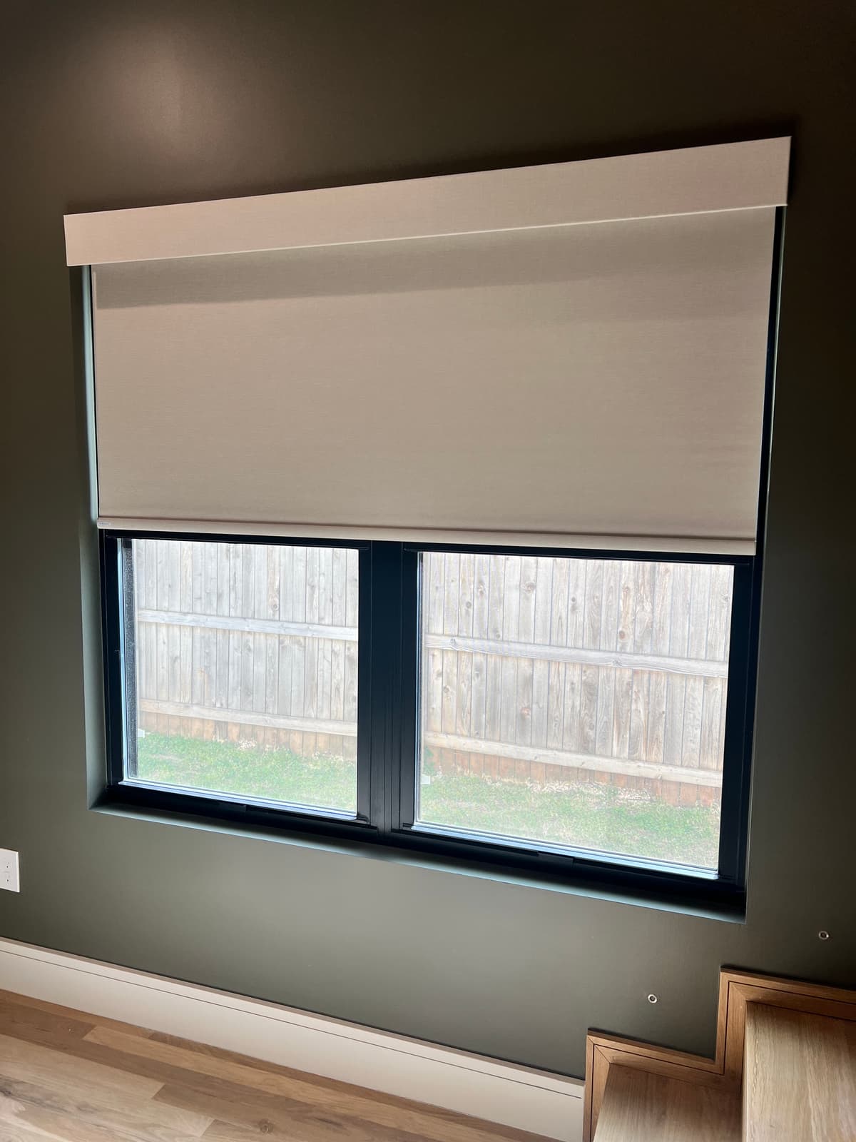 Cream roller shade half-drawn on modern window with dark green accent wall