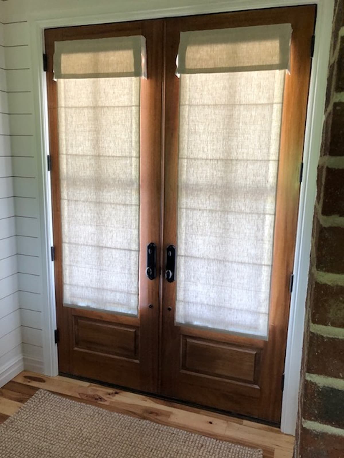 Linen roman shades on rustic wood French doors with brick surround