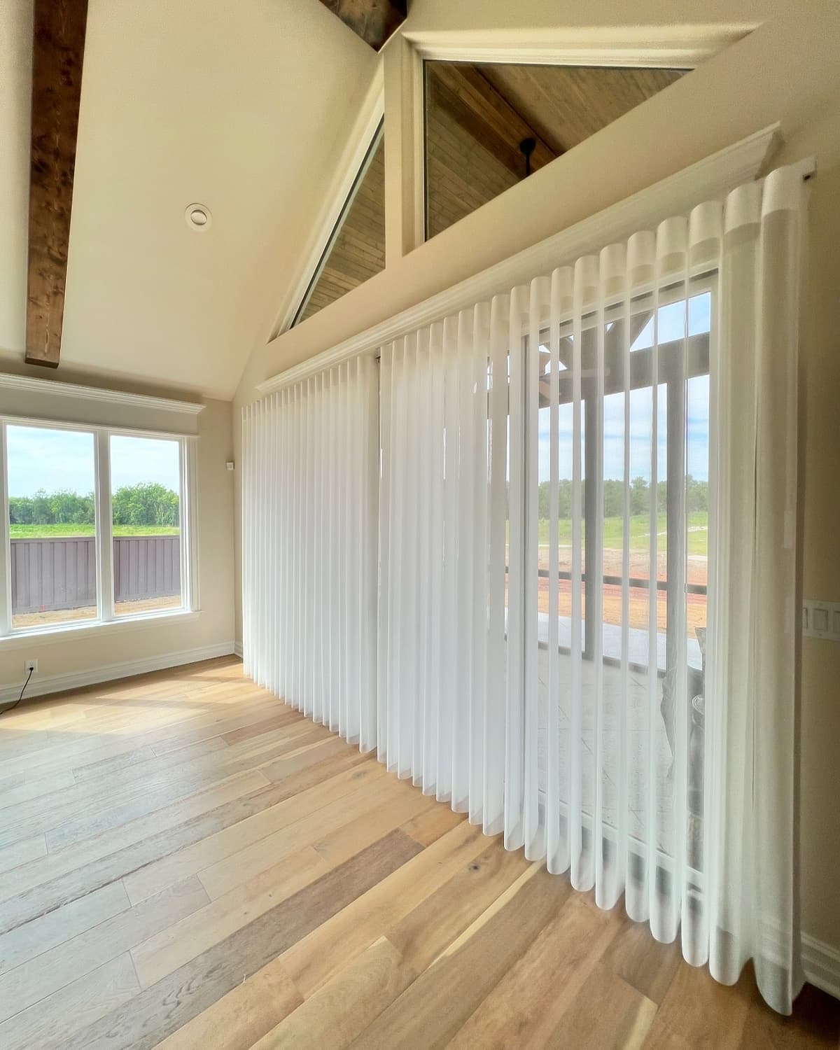 Sheer white drapery panels covering large glass doors in vaulted ceiling room with exposed beams