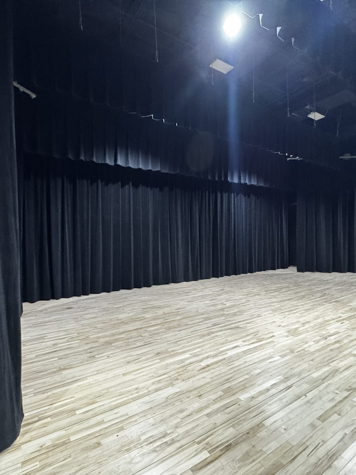 Floor-to-ceiling black stage drapery lining the walls of a performance studio with wood floors