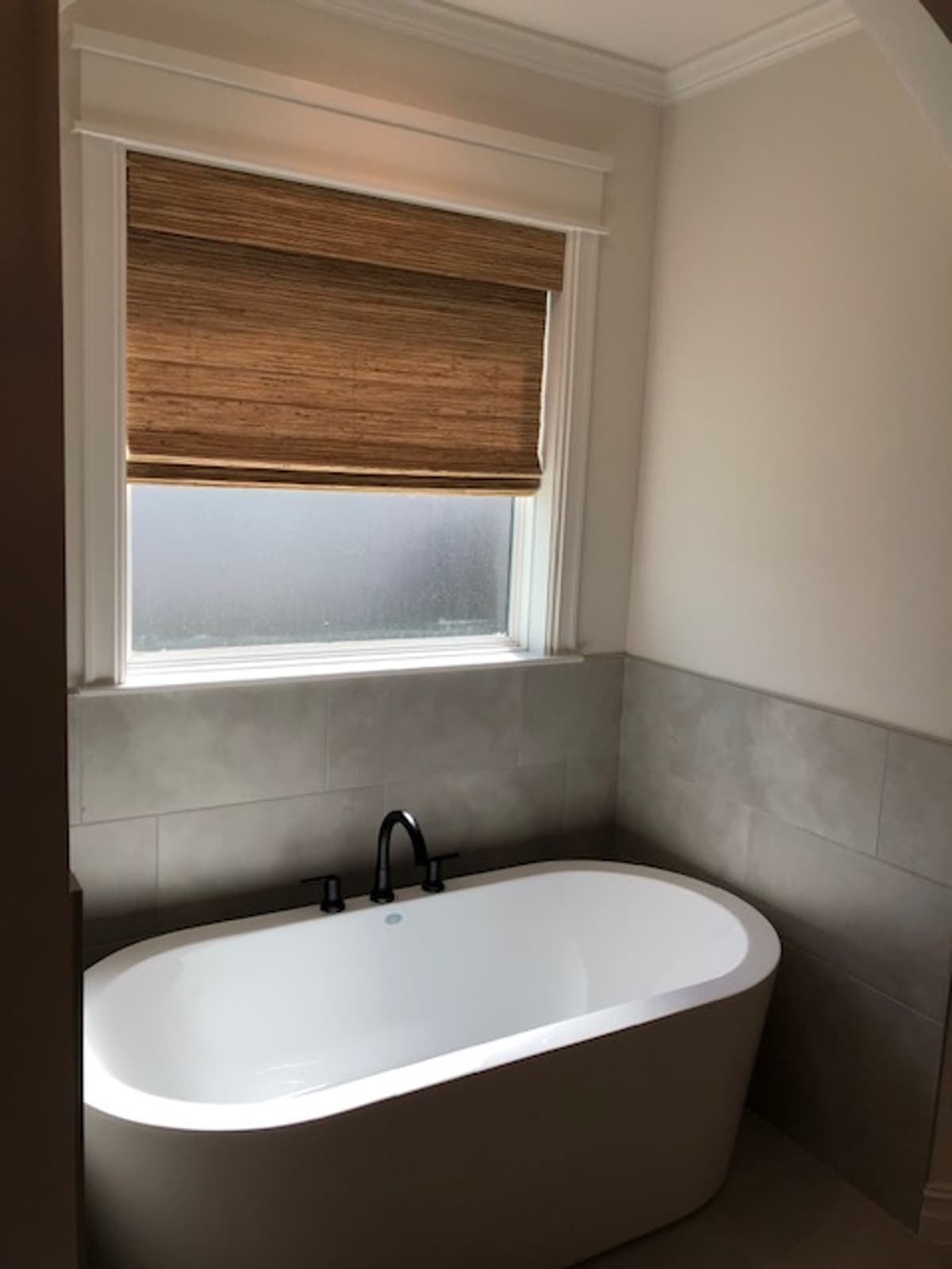 Woven bamboo roman shade above freestanding bathtub in modern bathroom
